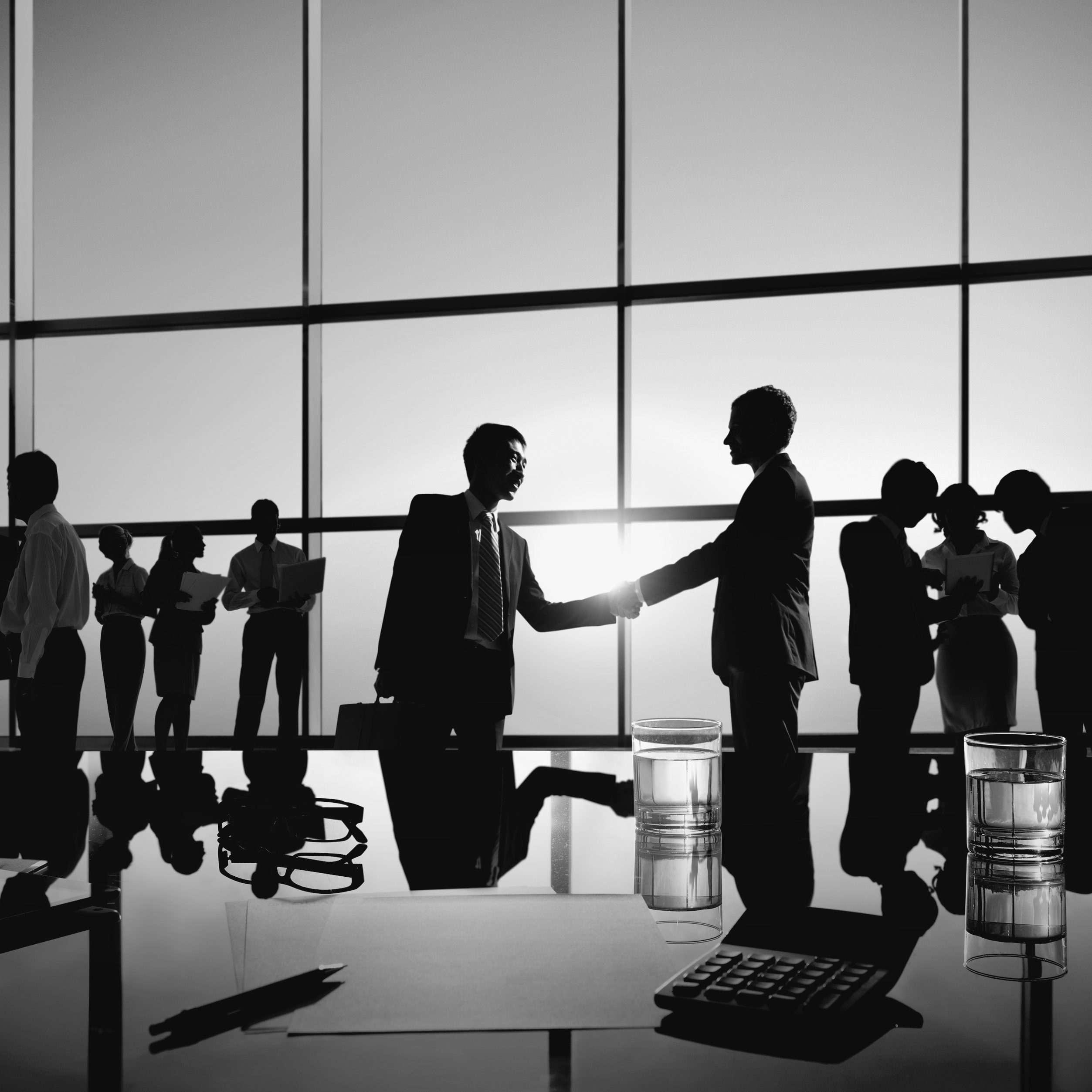 Two Businessmen Handshaking Together with Their Colleagues Two Businessmen Handshaking Together with Their Colleagues